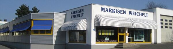 Das Geschäft Markisen Weichelt zeigt gelbe Fensterrahmen und blaue Markisen an der Fassade.