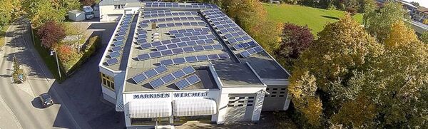 Auf dem Flachdach eines Firmengebäudes sind zahlreiche Solaranlagen für Photovoltaik installiert.