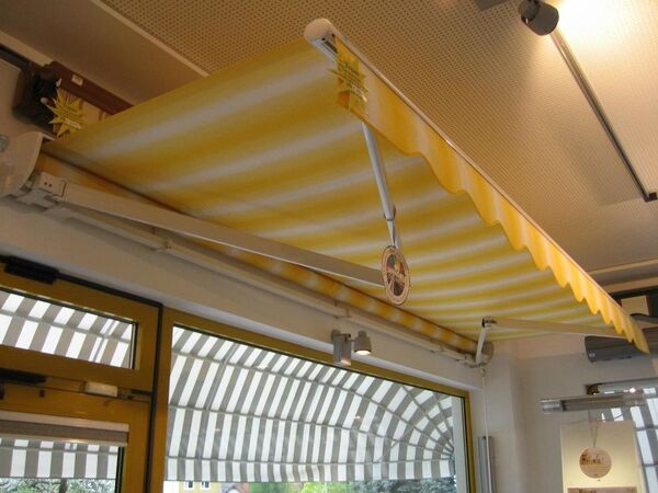 Gelb-weiß gestreifte Markise als Sonnenschutz über einem großen Fenster im Innenraum.