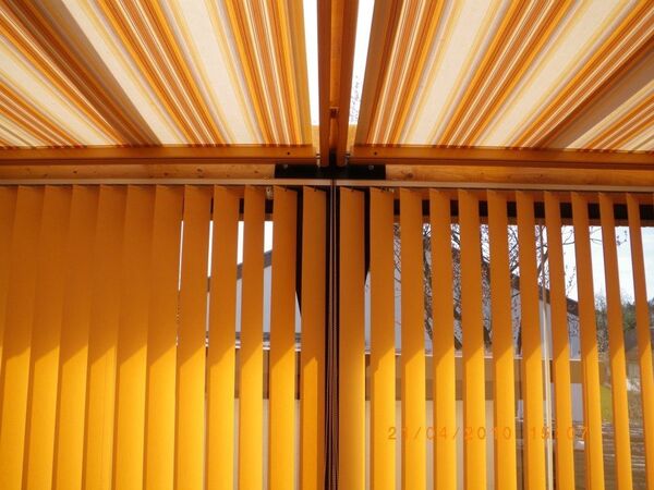 Gelbe Lamellenjalousie und Markise spenden Sonnenschutz auf einer Terrasse aus Holz.