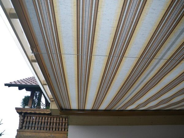 Gestreifte Markise als Sonnenschutz auf einer Terrasse mit Blick auf Holzgeländer.