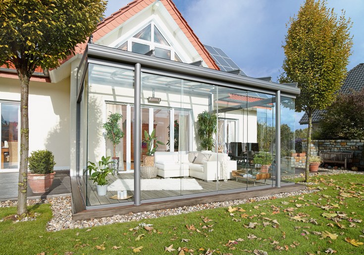 Moderner Wintergarten mit Glaswänden und gemütlicher Sitzecke am Einfamilienhaus im Grünen.